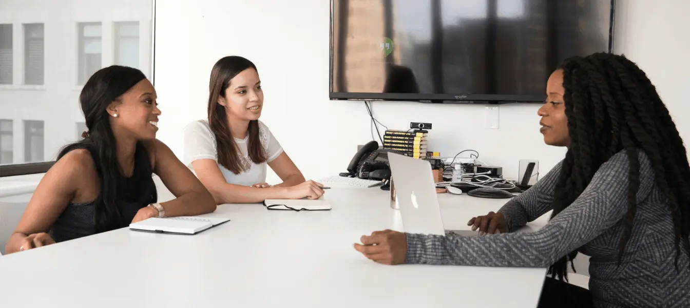 Three female employees having a meeting at a desk in an office.